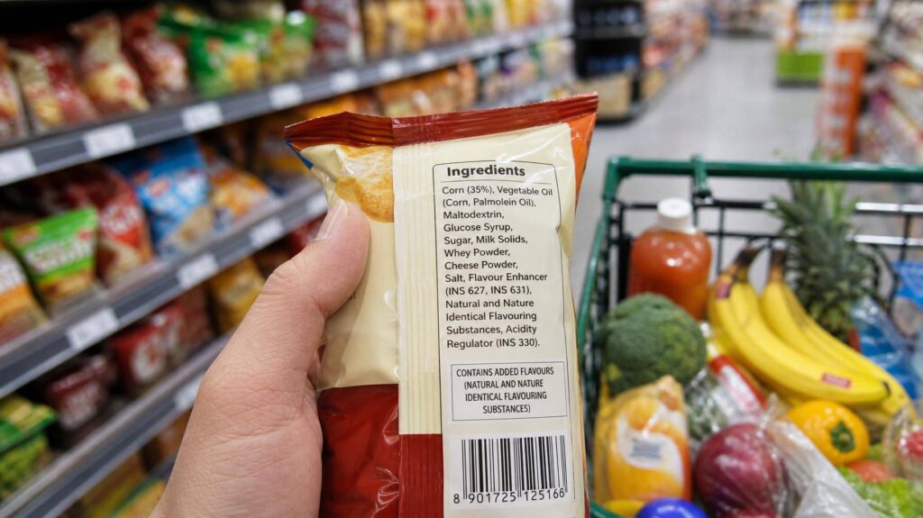 Mão segurando produto com rótulo de açúcares escondidos em supermercado